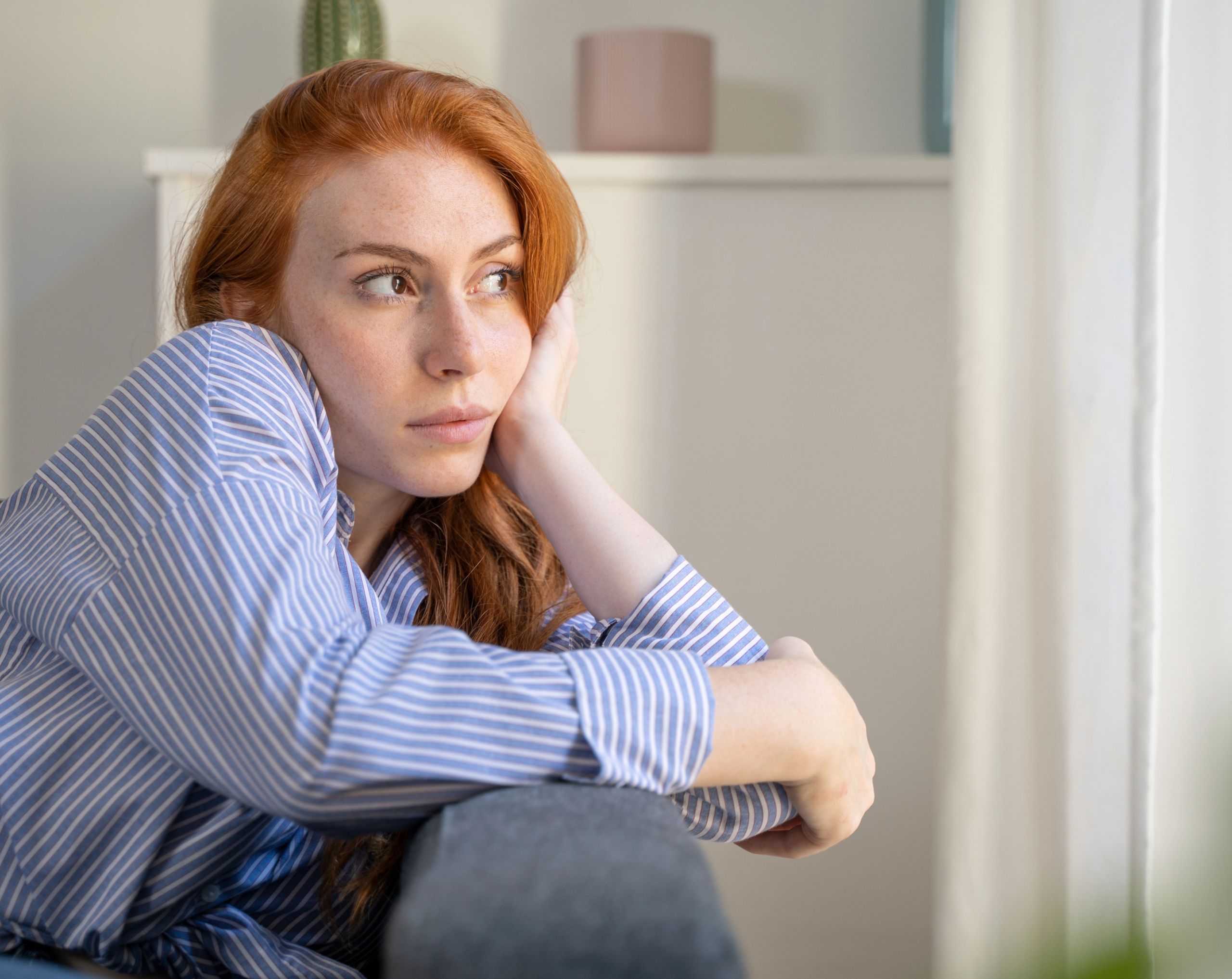 Mujer de mediana edad sentada en un sofá soñando despierta, reflejando ensoñación excesiva.