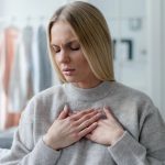 Mujer de mediana edad toca su pecho a la altura del corazón por dolor, síntoma asociado a la miocardiopatía dilatada.