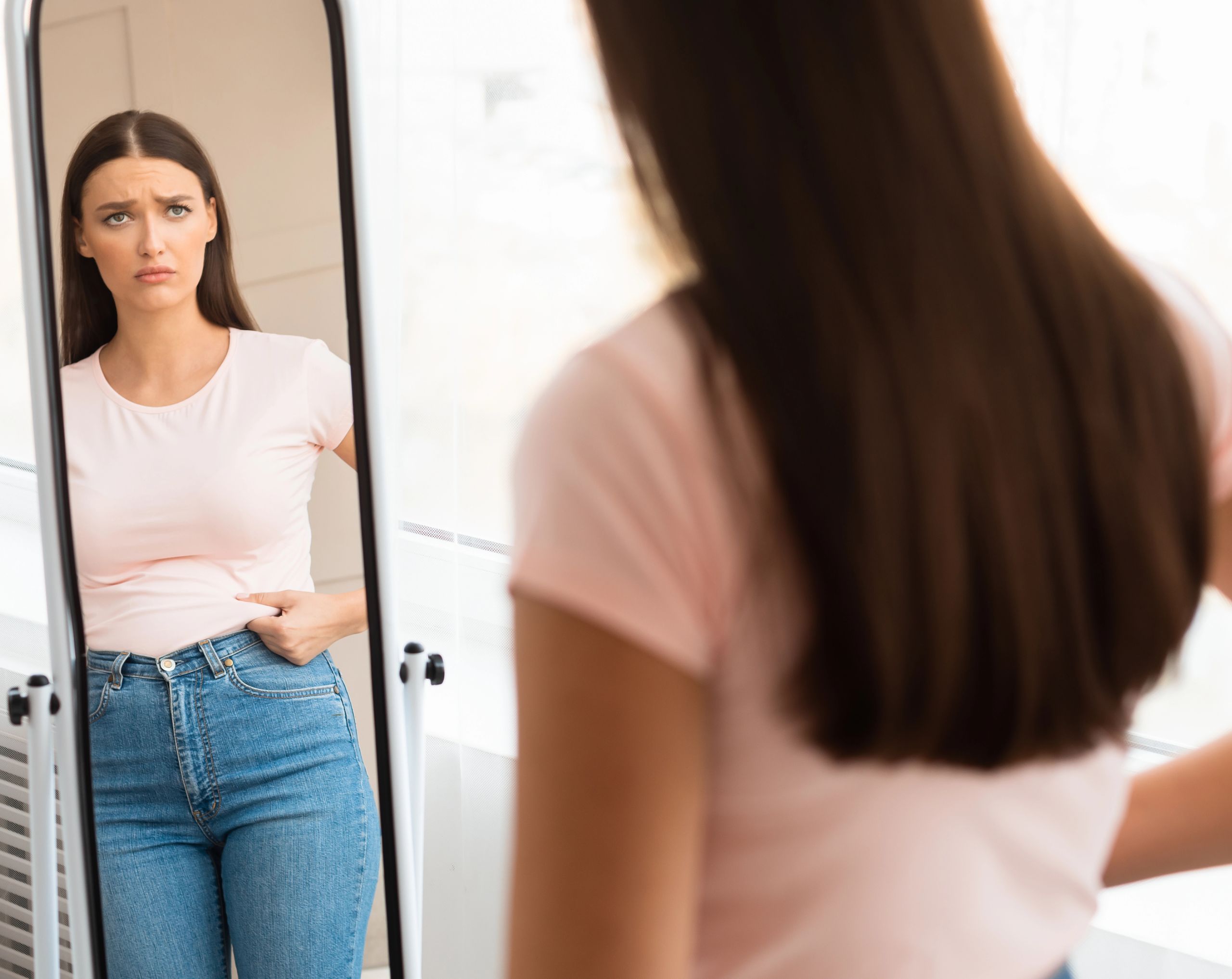 Mujer de mediana edad frente al espejo, observando su cuerpo por aumento de peso, un posible síntoma del Síndrome de Cushing.