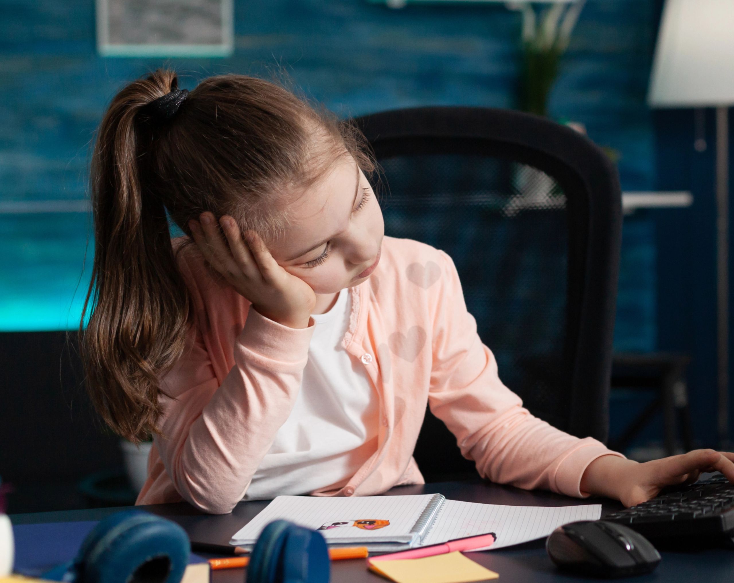 Niña pequeña sentada frente a una computadora con expresión distraída, mostrando dificultad para concentrarse, posible síntoma de TDAH.