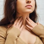 Mujer de mediana edad tocándose la zona del cuello donde se encuentra la tiroides, mostrando posibles síntomas de Tiroiditis de Hashimoto.