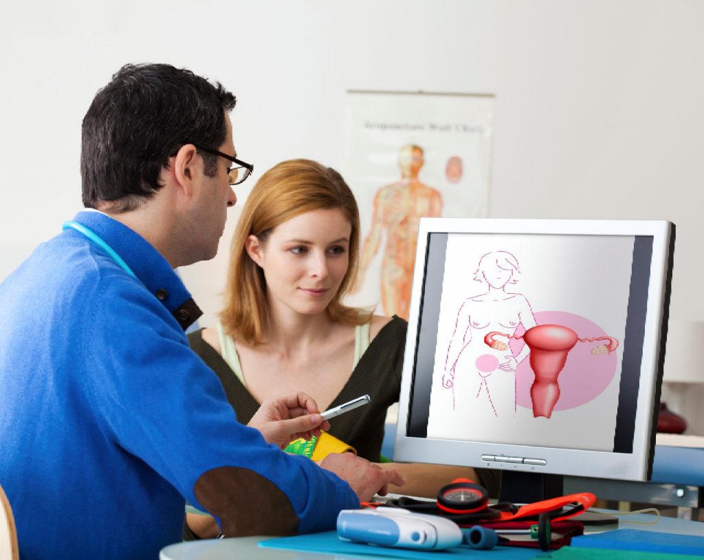 Médico ginecólogo le explica a su paciente sobre el prolapso uterino dentro de su consultorio, señalando una imagen en la computadora.
