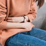 Mujer con dolor de útero se abraza el vientre por posible prolapso uterino.