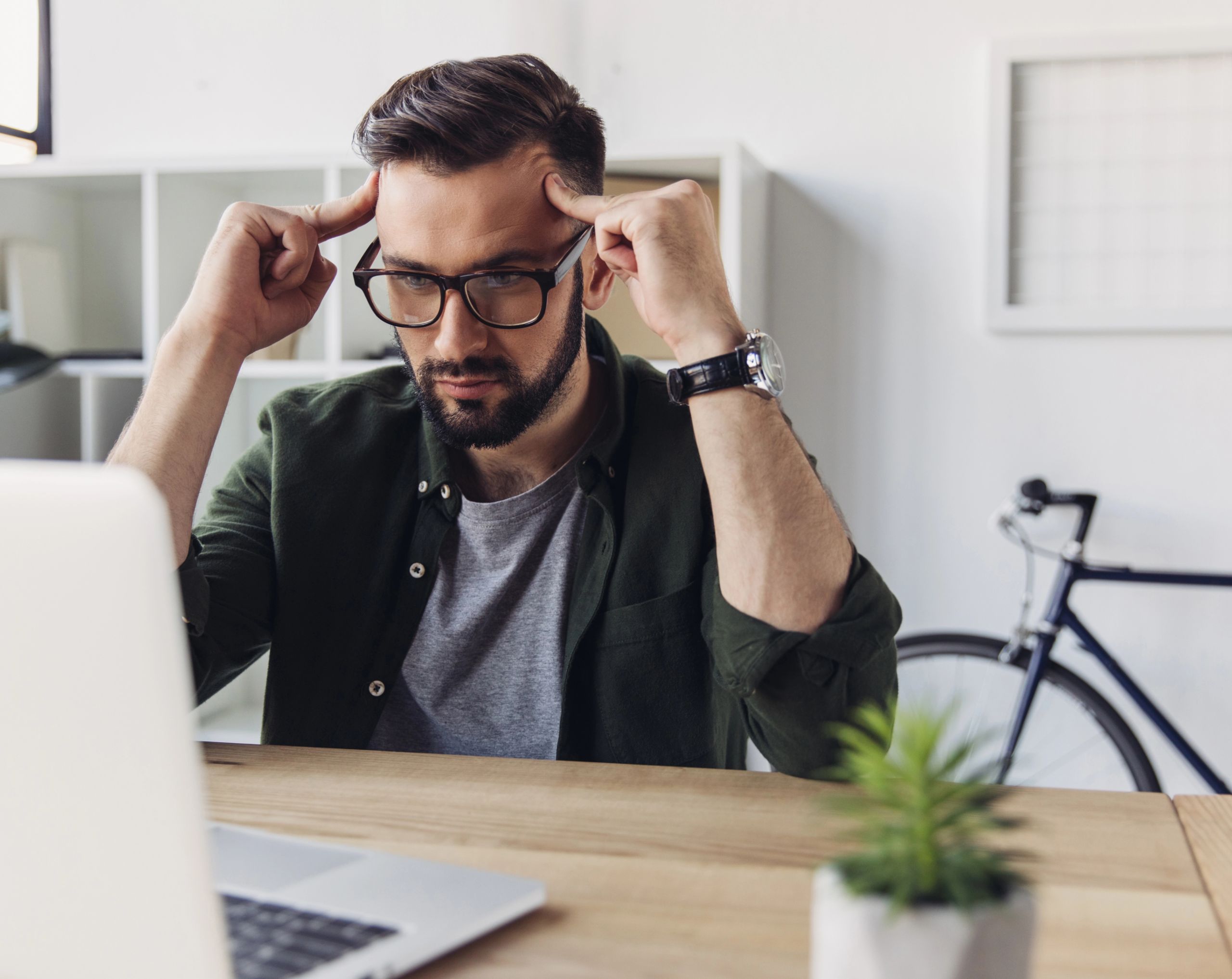 Hombre de mediana edad sentado frente a una computadora, con ambas manos en las sienes mostrando frustración por problemas de concentración, posible síntoma de TDAH.