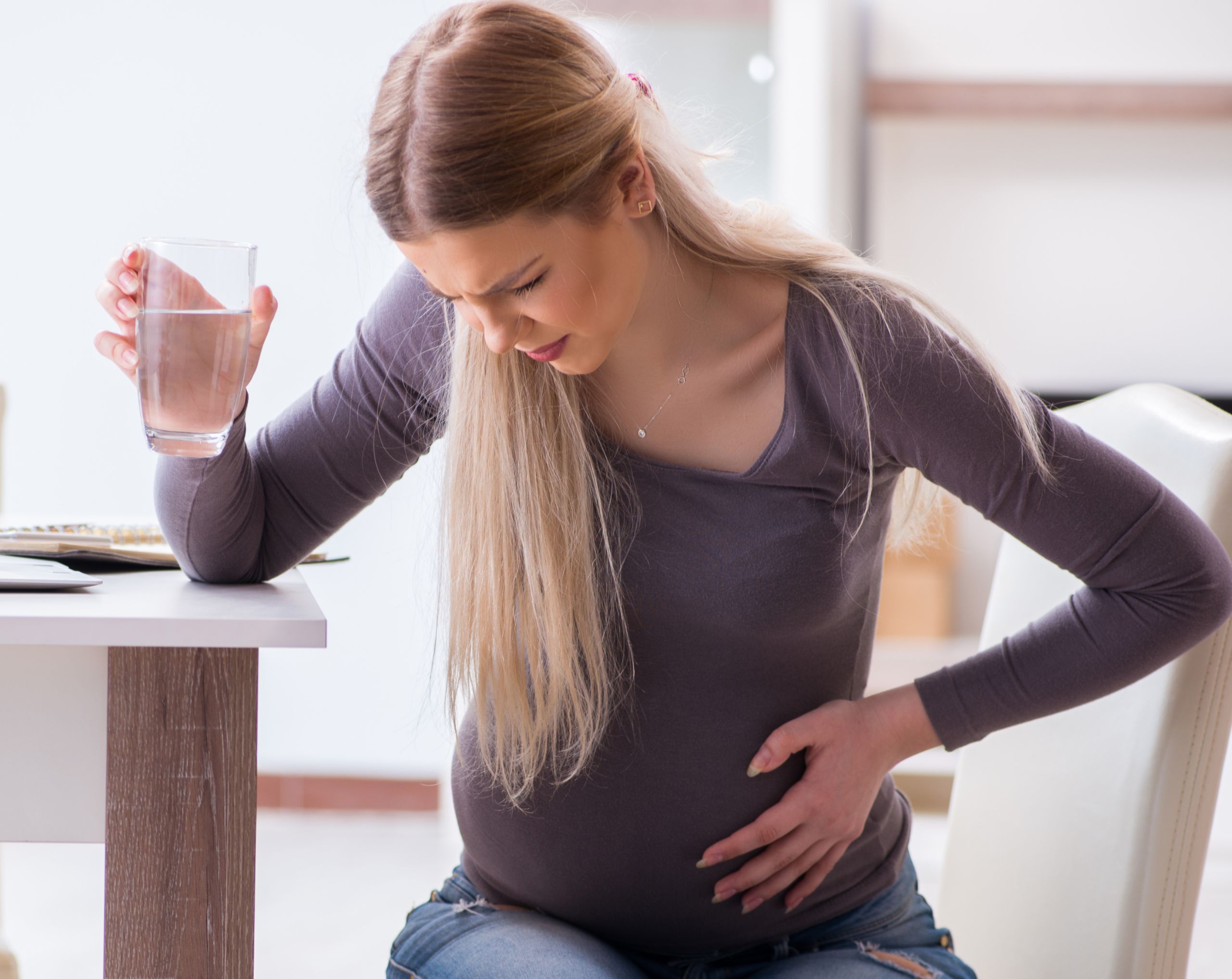 Mujer joven con 30 semanas de embarazo sentada en el comedor, muestra una leve expresión de dolor por las contracciones de Braxton Hicks.
