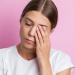 Mujer adulta de mediana edad sostiene con una mano el lado derecho de su rostro por contracciones involuntarias visibles por un espasmo hemifacial.