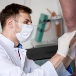 Médico angiólogo revisa las piernas de una paciente en el consultorio en busca de indicios de trombosis venosa.