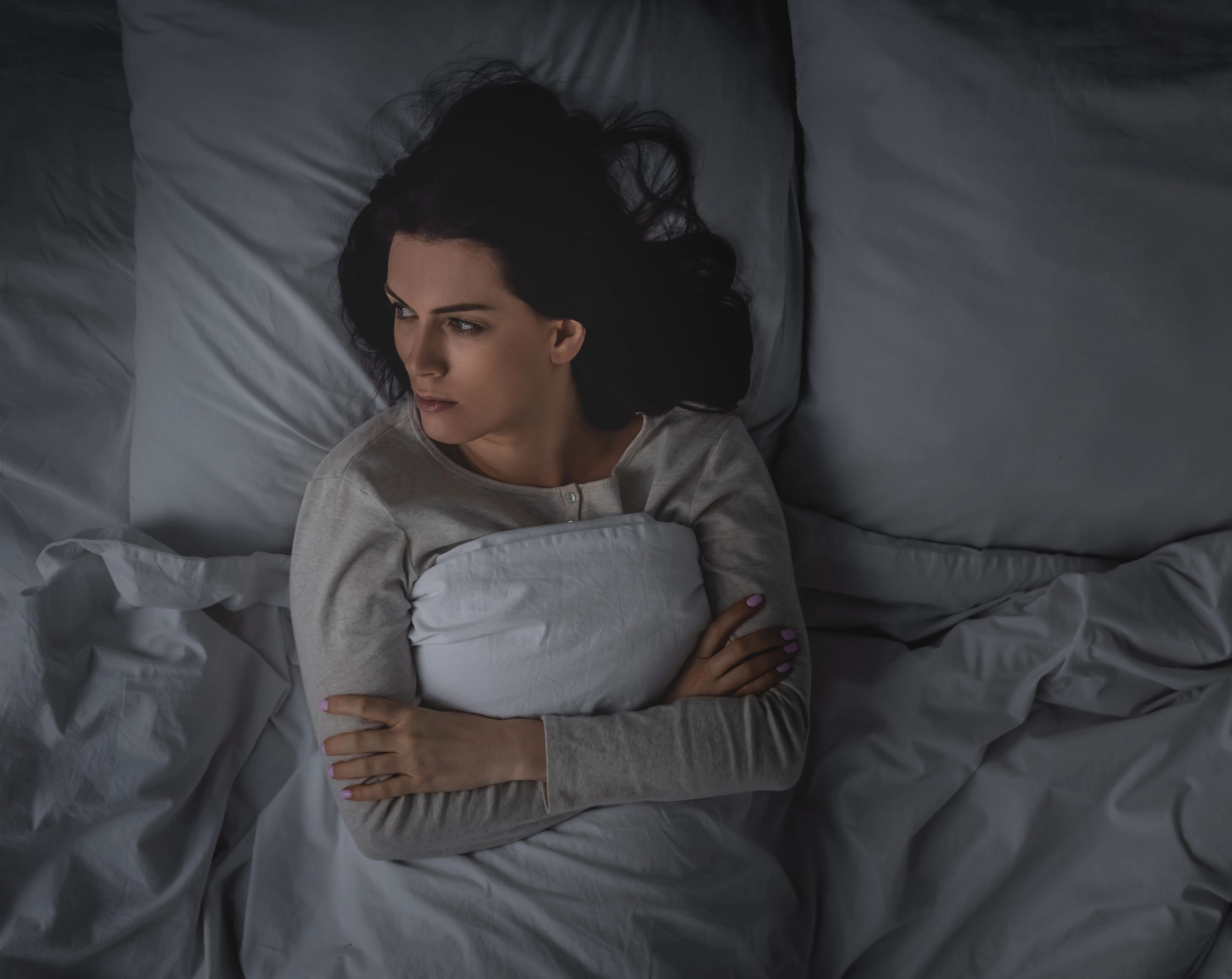 Mujer recostada en su cama a oscuras, incapaz de dormir debido a niveles bajos de melatonina.