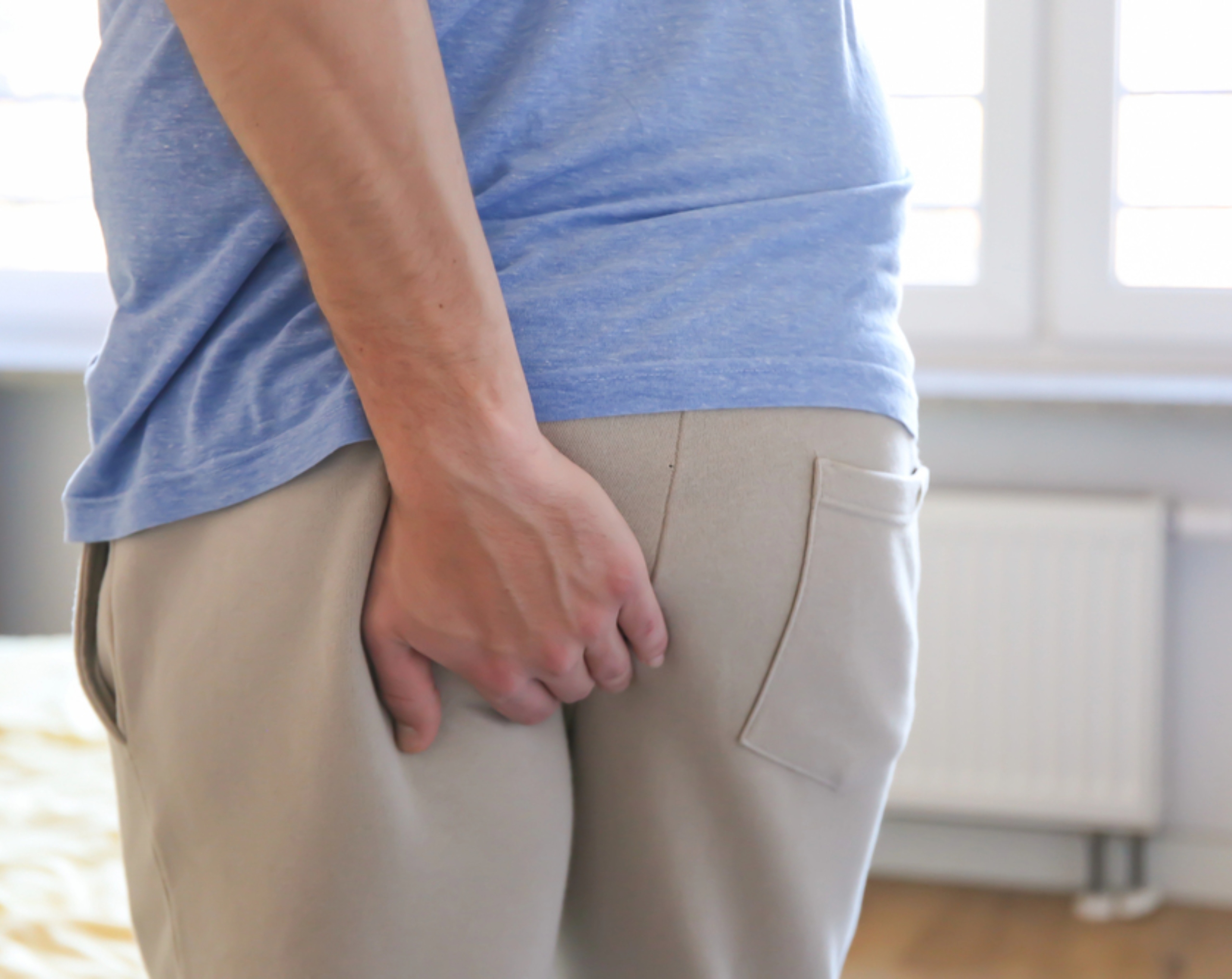 Hombre adulto mayor coloca su mano en la zona baja de la espalda debido al dolor provocado por un absceso perianal.