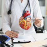 Cardióloga señala una arteria del corazón con una pluma mientras explica a un paciente el tratamiento con stent coronario.