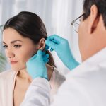 Otorrinolaringólogo examina el oído de una mujer con ambas manos durante una revisión para evaluar si requiere una timpanoplastia.