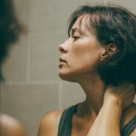 Mujer de edad media se mira al espejo para revisarse el cuello en busca de acantosis nigricans.