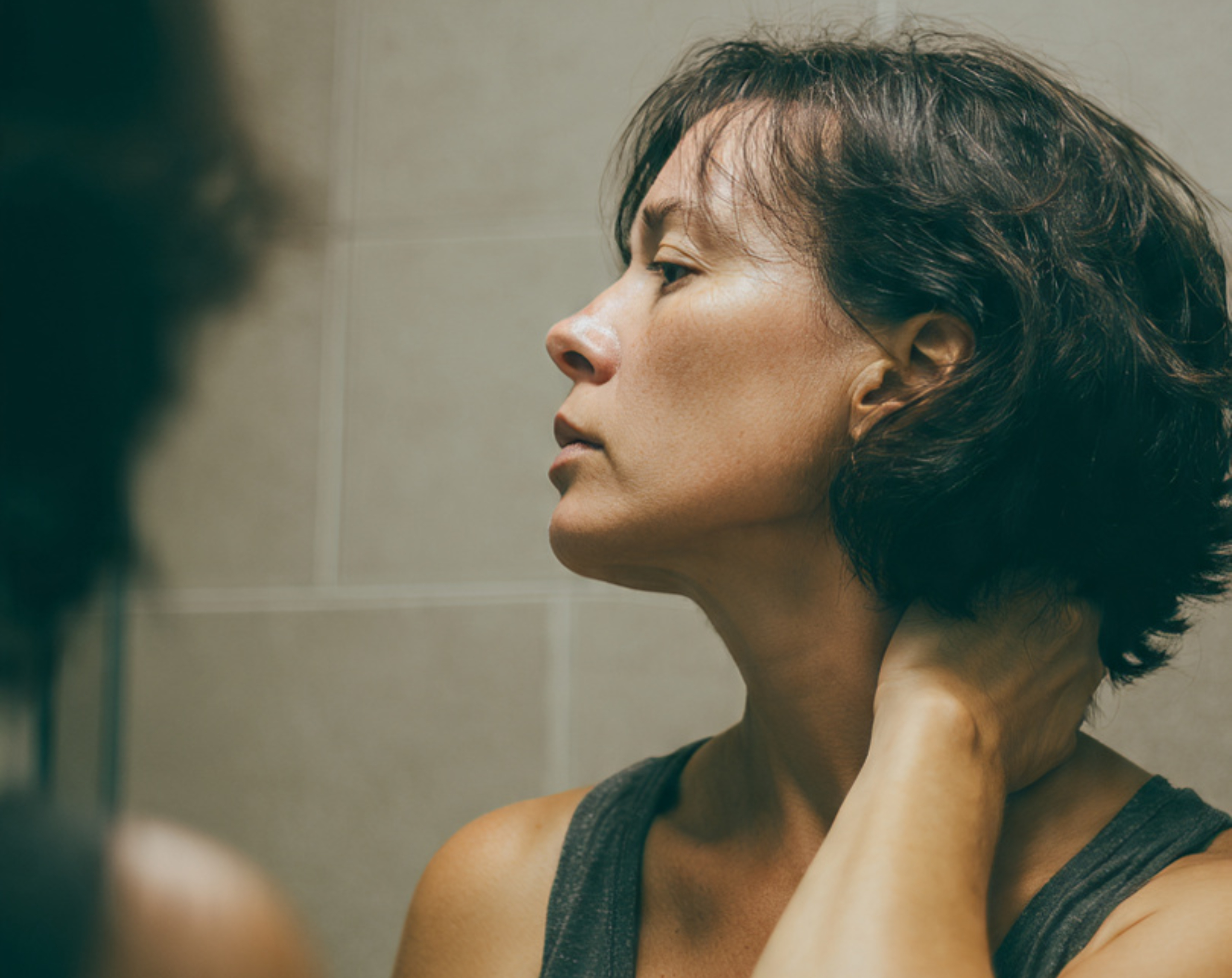 Mujer de edad media se mira al espejo para revisarse el cuello en busca de acantosis nigricans.
