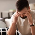 Hombre de edad media se toca las sienes manifestando dolor de cabeza por resaca.