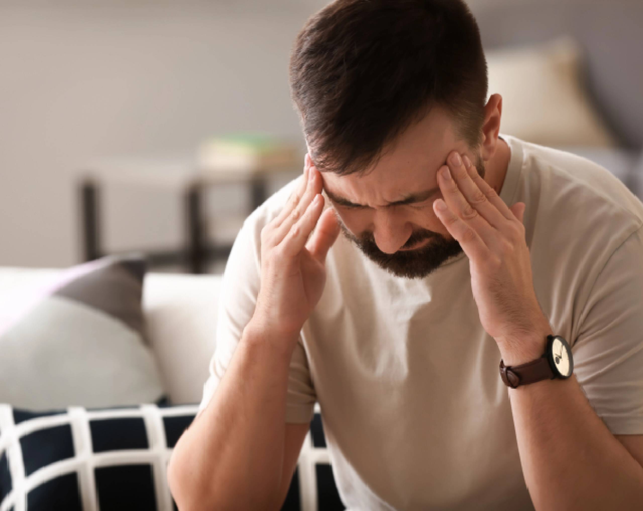 Hombre de edad media se toca las sienes manifestando dolor de cabeza por resaca.