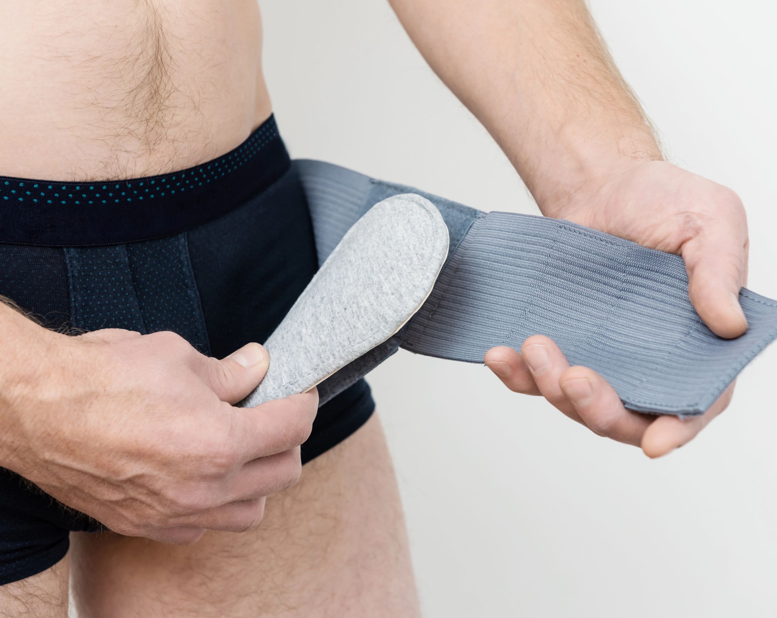 Hombre de mediana edad, en ropa interior, coloca una malla de soporte en la parte baja del abdomen para aliviar los síntomas de una hernia inguinal.