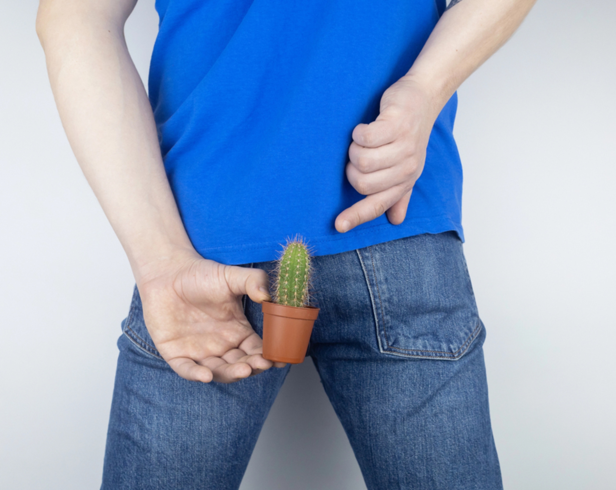 Hombre de mediana edad sostiene con su mano izquierda una maceta pequeña con un cactus de espinas, utilizado como metáfora del dolor y las molestias de un absceso perianal.