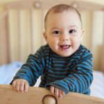 Bebé dentro de su cuna mostrando la lengua con parches blancos característicos del algodoncillo en bebés.