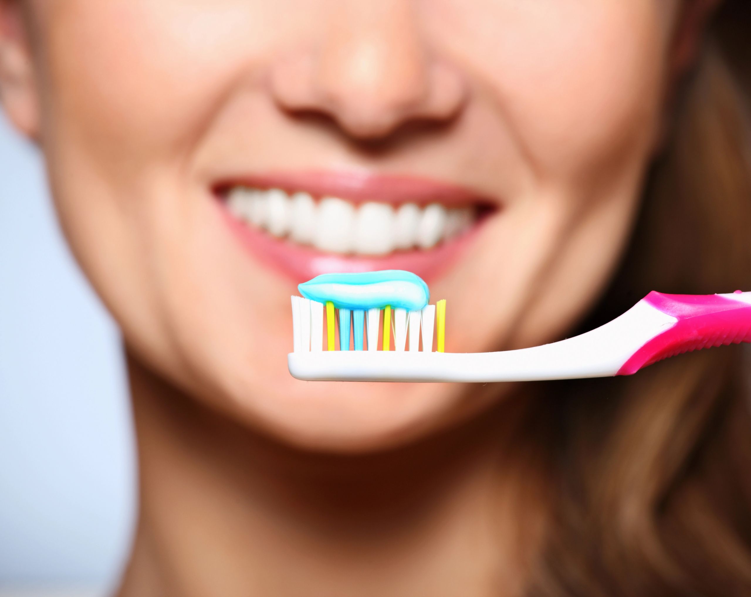 Mujer de mediana edad sonriendo junto a un cepillo de dientes, representando la buena higiene bucal para prevenir el algodoncillo en adultos.