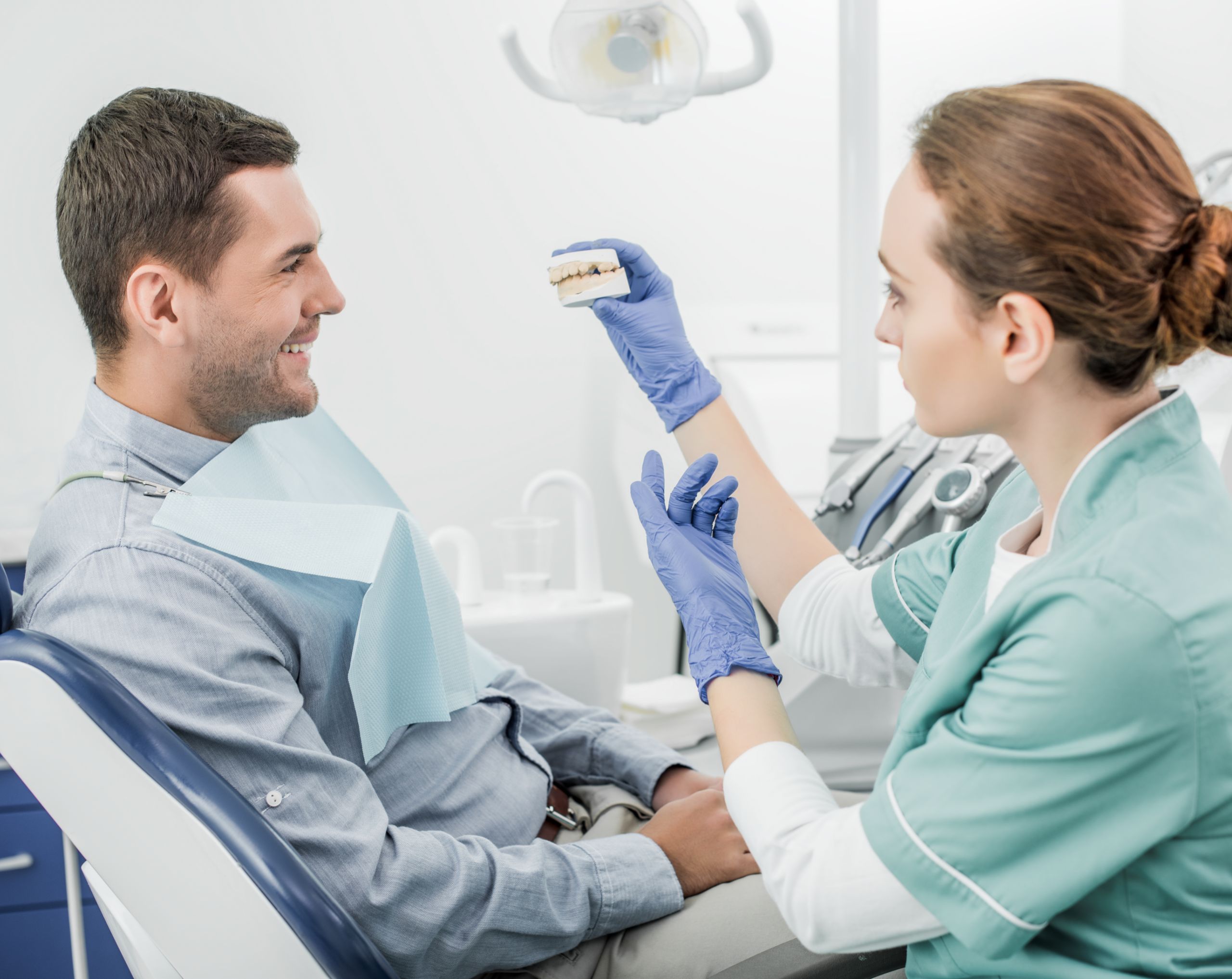 Ortodoncista sostiene un modelo anatómico 3D de la mordida con ortodoncia frente a la paciente.