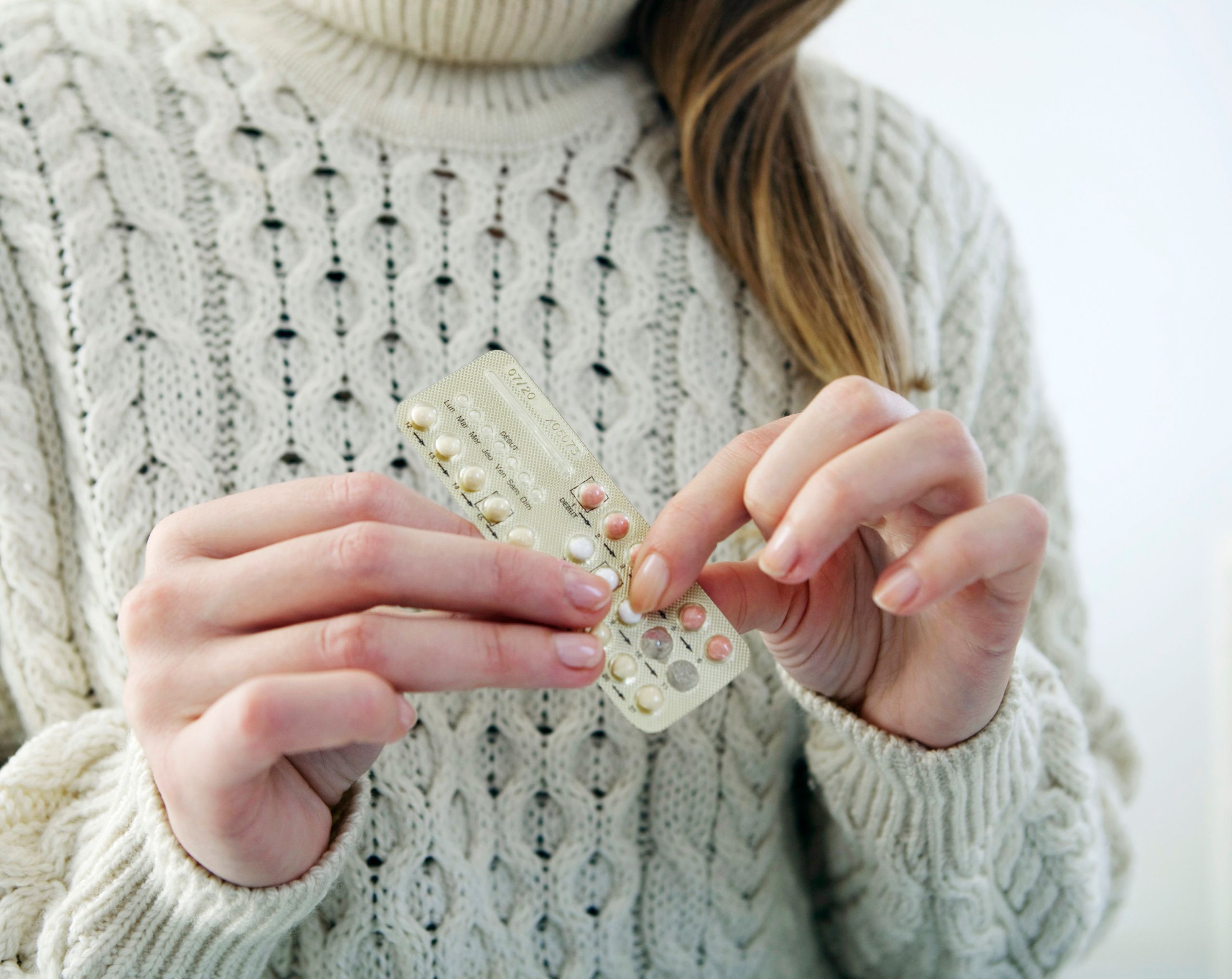 ujer joven sostiene pastillas anticonceptivas hormonales con ambas manos.