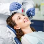 Odontólogo examina la mordida de paciente con ortodoncia fija usando instrumental dental en consulta.