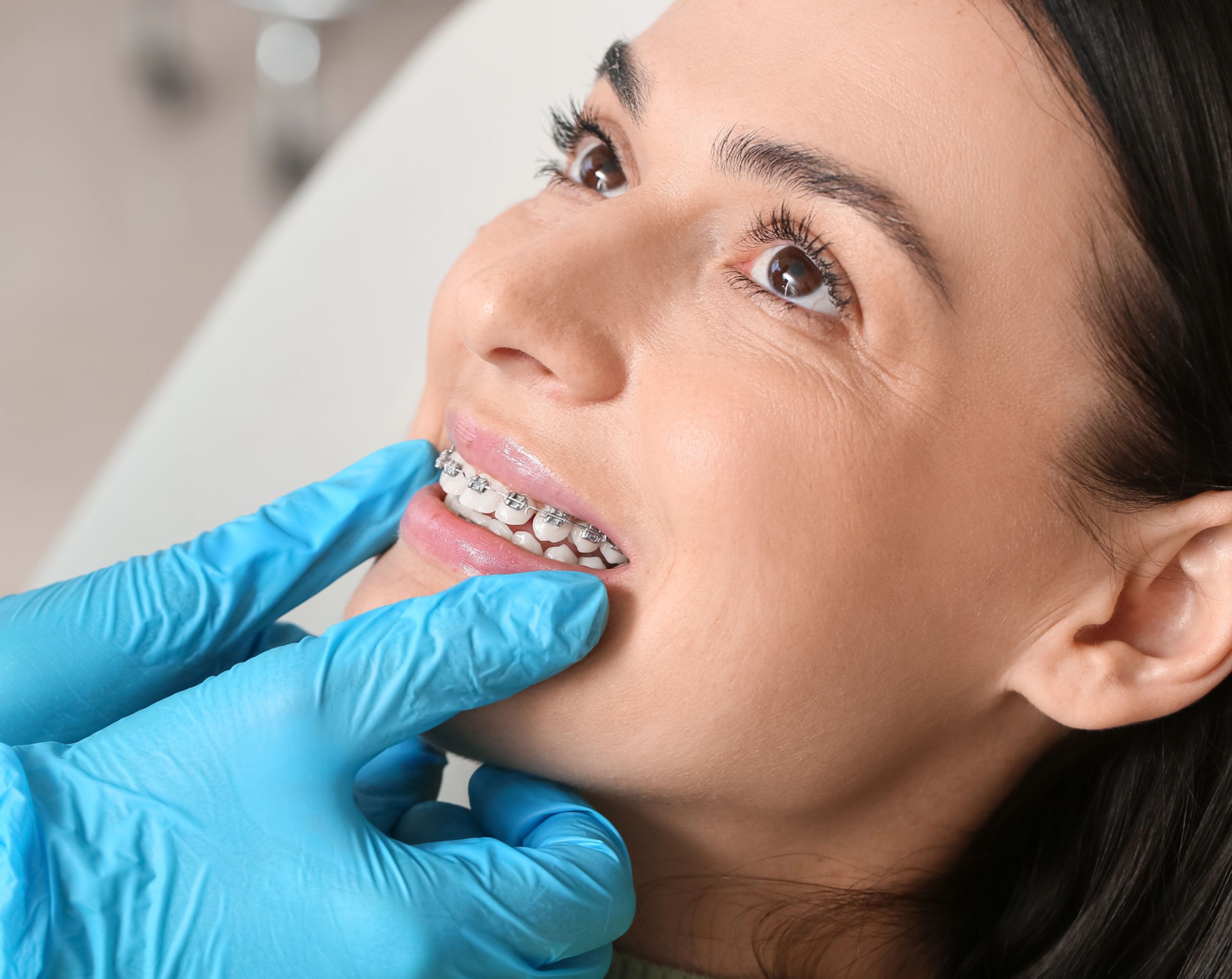 Mujer joven recostada en la camilla del consultorio mientras el ortodoncista revisa su ortodoncia.