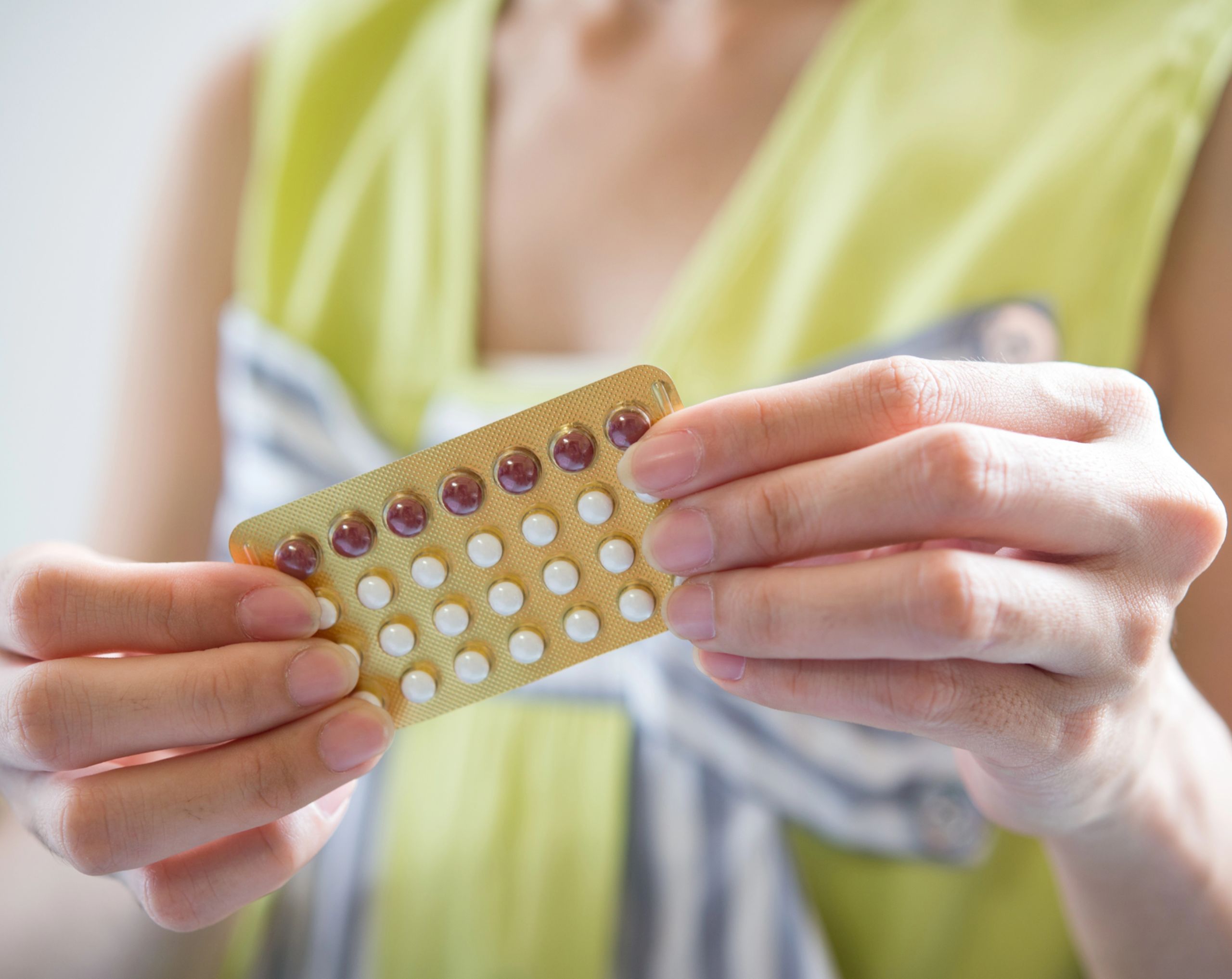 Mujer adulta joven sostiene un blíster de pastillas anticonceptivas hormonales con ambas manos. 