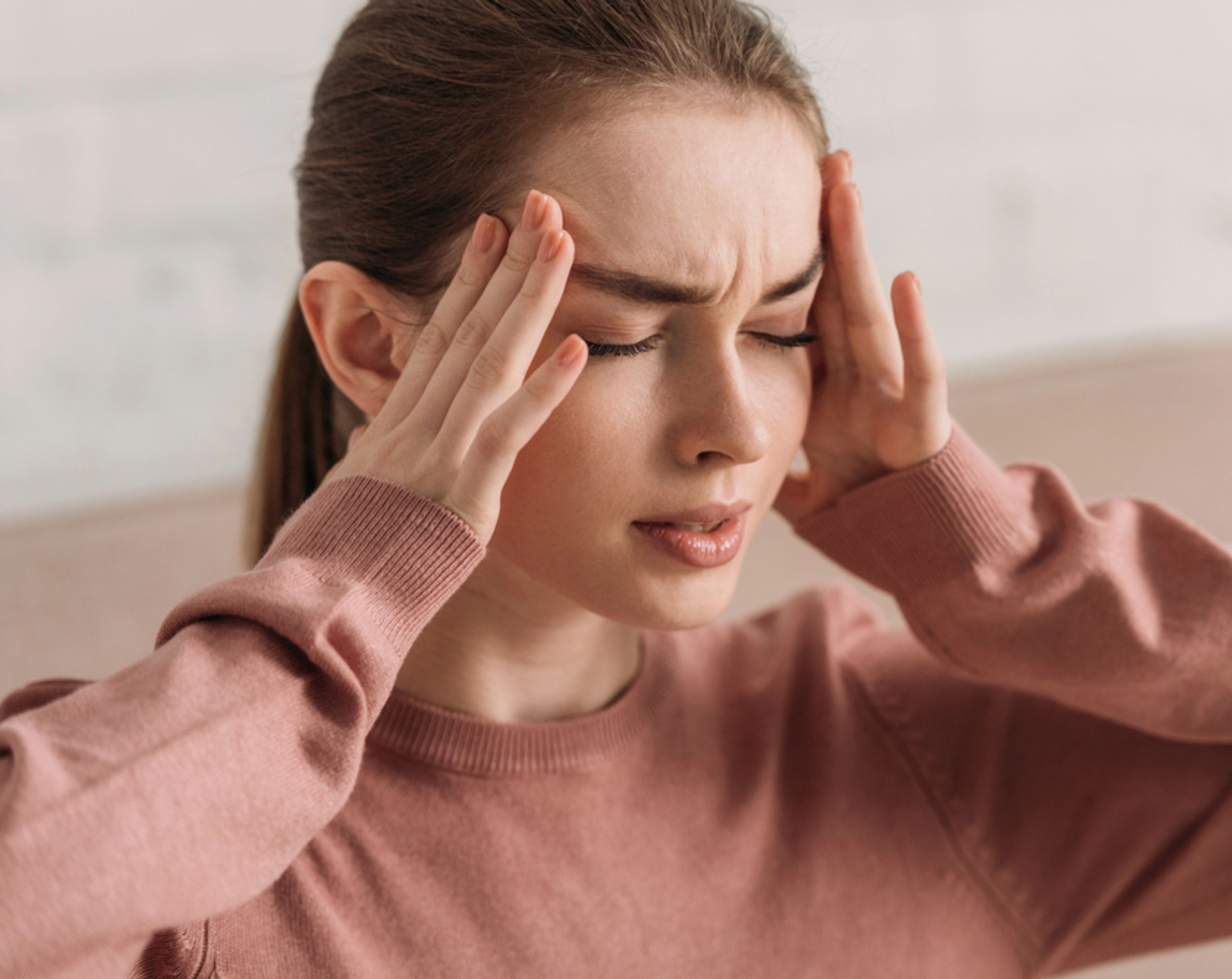 Mujer joven con dolor de cabeza intenso, presionando sus sienes, posible síntoma de meningitis.