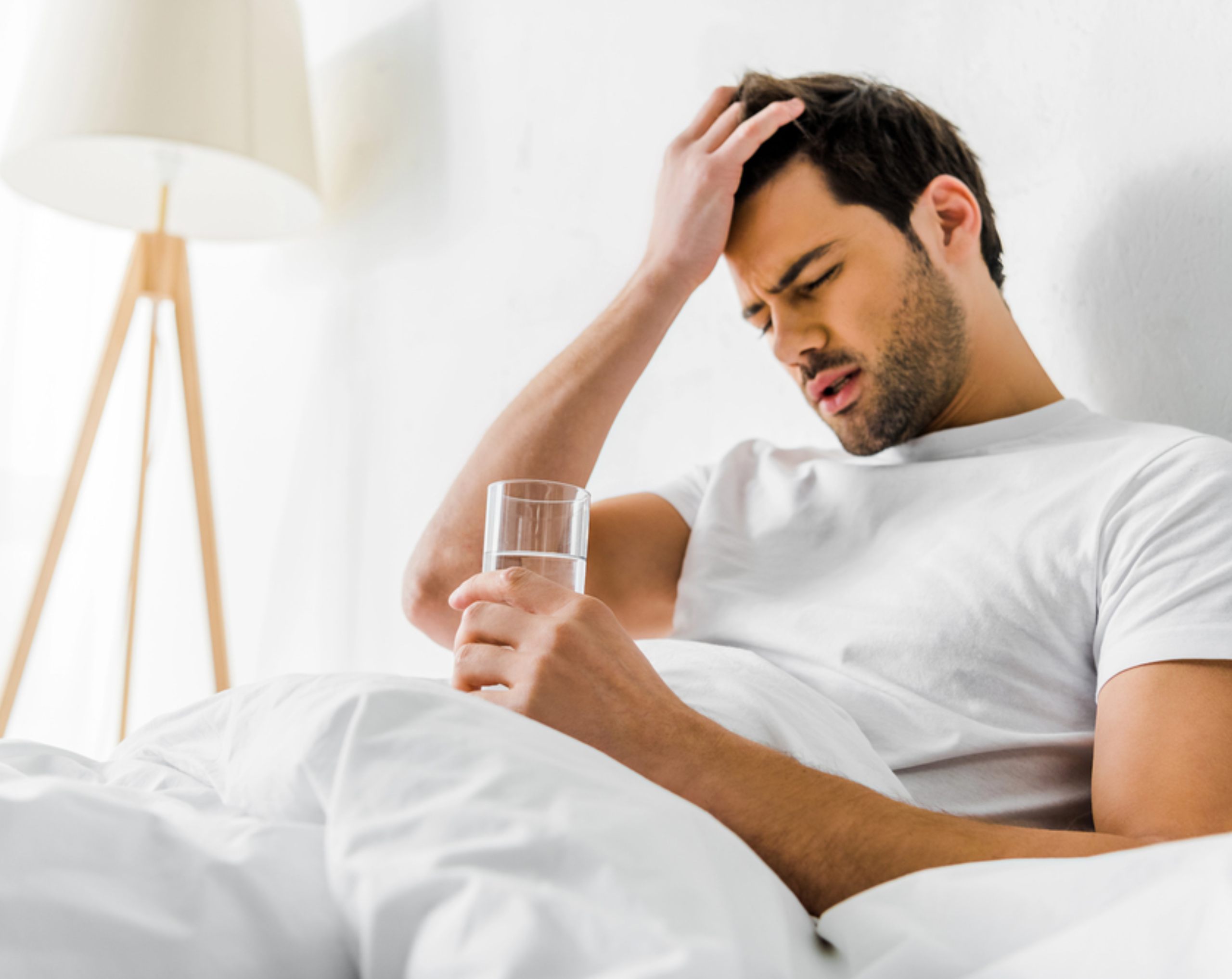 Hombre recostado en una cama sosteniendo un vaso con agua, ilustrando el reposo como parte del tratamiento de la meningitis.
