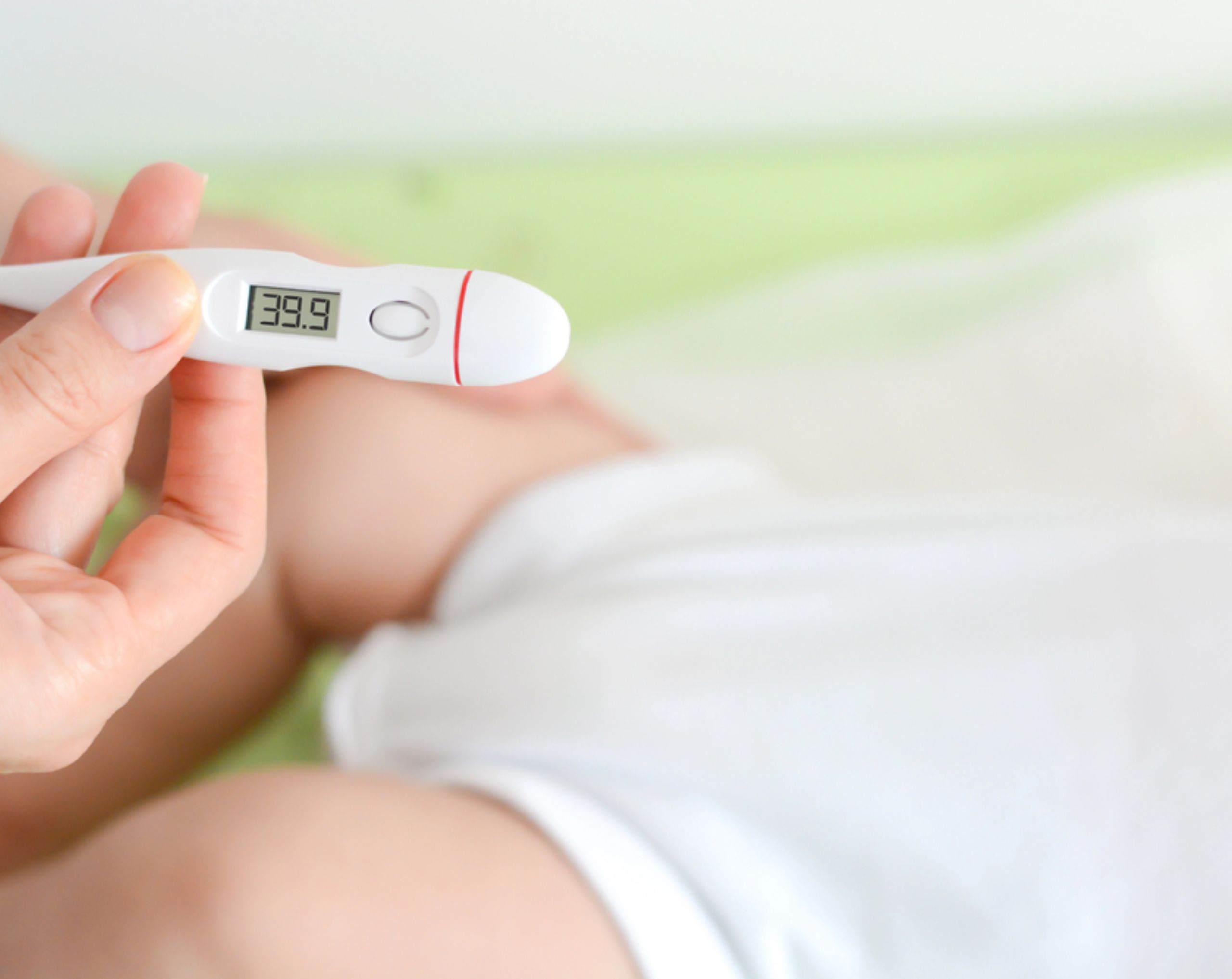 Niño pequeño acostado con fiebre alta mientras su madre sostiene un termómetro, posible síntoma de meningitis en bebés.