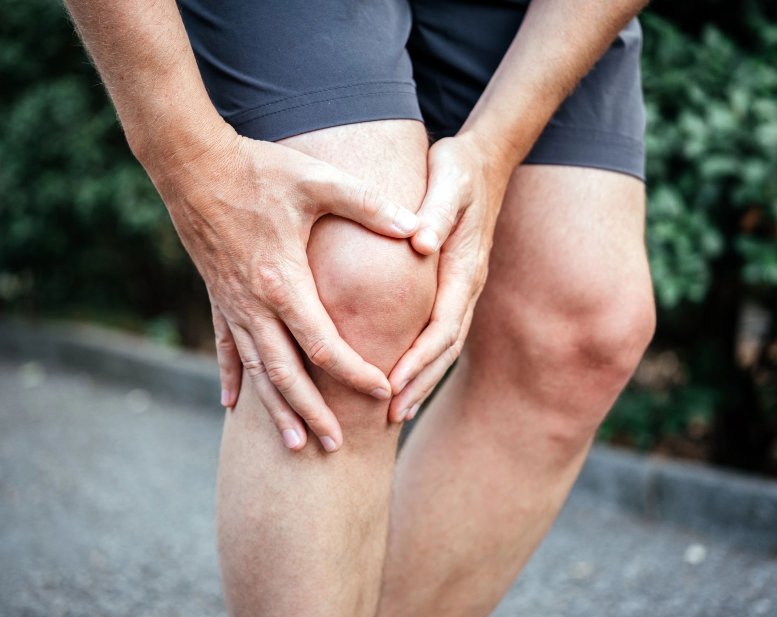 Hombre sostiene su rodilla con ambas manos por posible lesión durante actividad física.