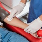 Enfermero coloca algodón en el brazo de un donador altruista después de una donación de sangre, mientras el paciente sostiene una pelota de goma utilizada para favorecer el flujo sanguíneo durante el procedimiento.