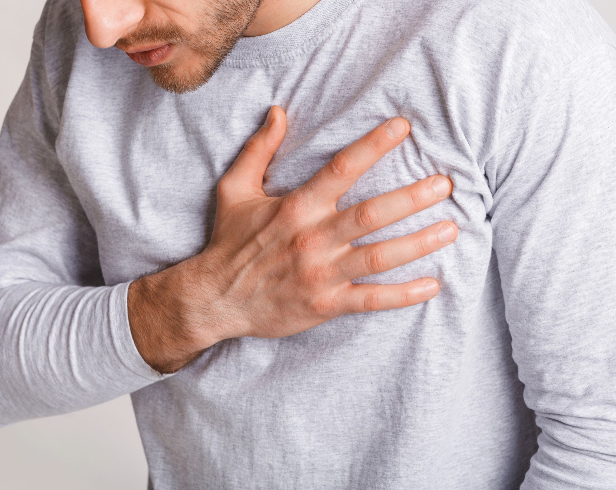 Hombre joven se lleva la mano al pecho por dolor, posible síntoma de muerte súbita cardíaca en atletas jóvenes. 