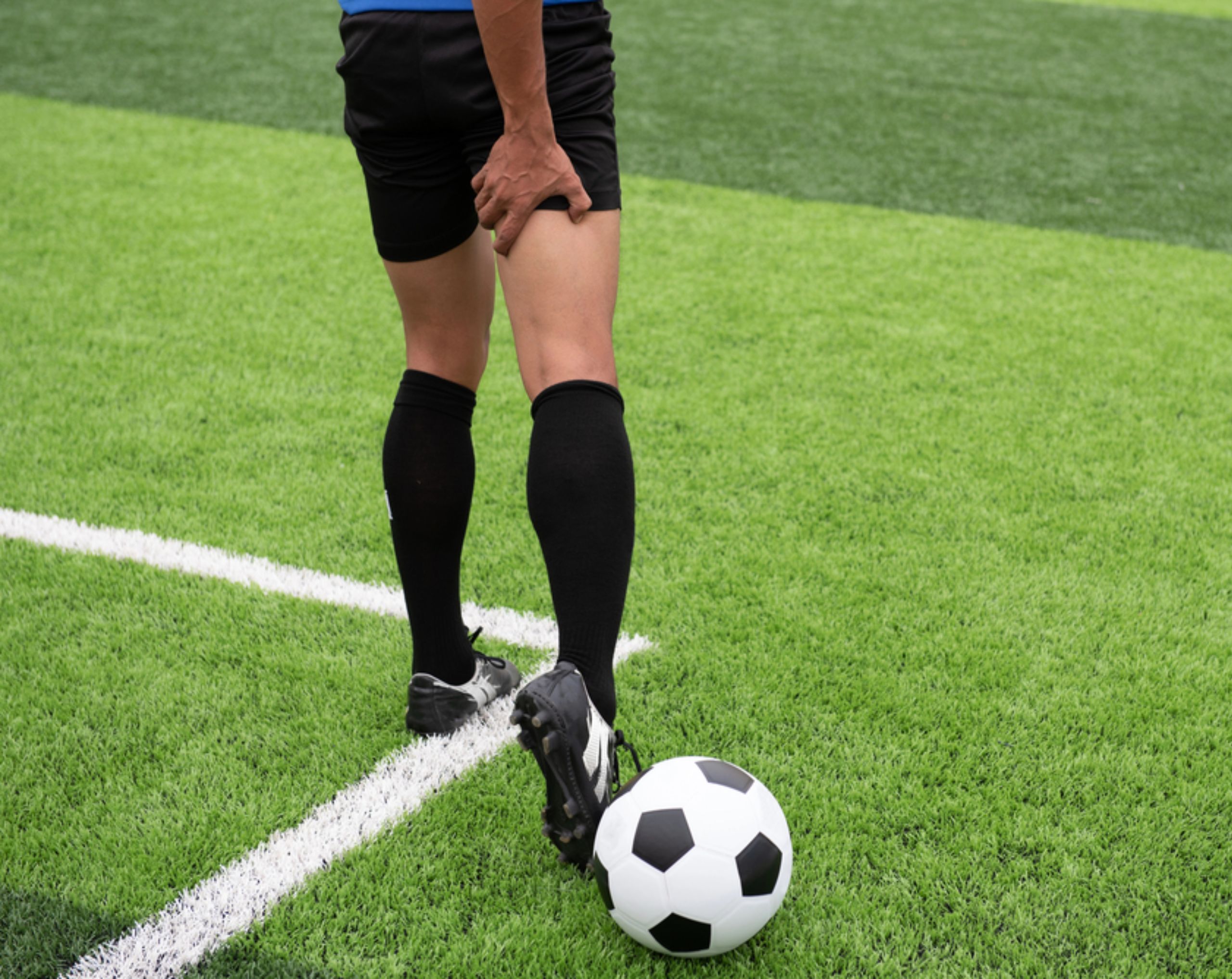 Jugador de futbol con dolor en la pierna después de una lesión deportiva en la cancha.