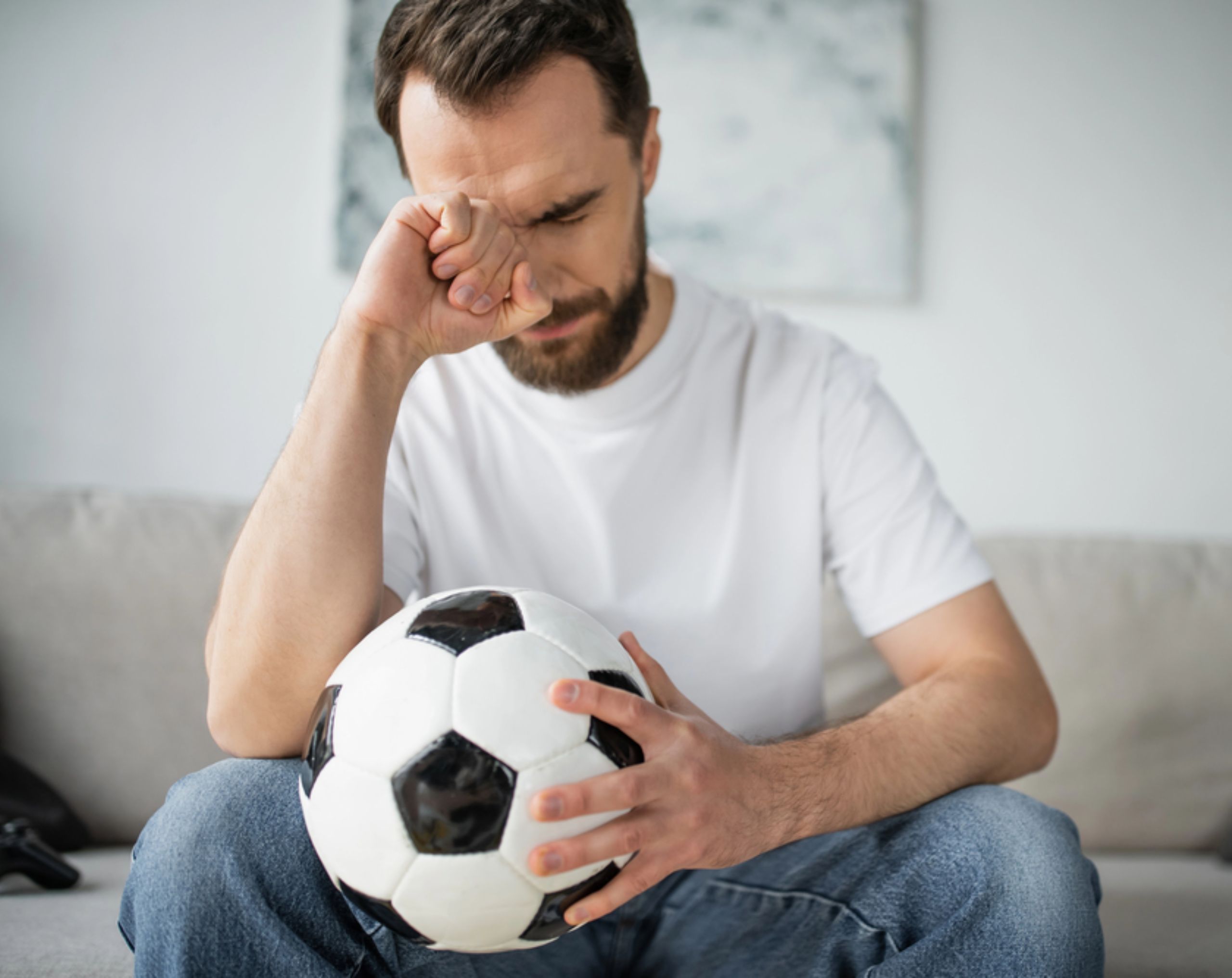 Hombre aficionado del futbol con expresión de tristeza sentado en la sala de su casa viendo un partido de futbol.