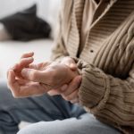 Hombre adulto mayor que sostiene una mano con la otra para controlar los trastornos del movimiento.